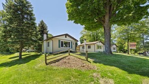 A two-story house with a wooden fence in front, surrounded by green grass and trees.