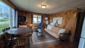 A cozy room with a wooden interior, a dining table with chairs, a sofa, a TV, and a window with a view of the outside. - Cozy Cabin for Two w/ access to Pickleball (Chippewa Lake)