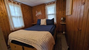 A cozy room with wooden walls, a bed with a blue and white blanket, a heart-shaped pillow, and a sign that says 'Sweet Dreams.'