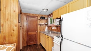 A compact kitchen with wooden walls, a white refrigerator, a stove, and a sink.