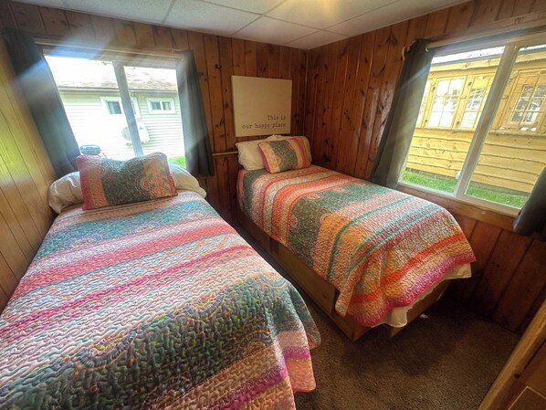 Acogedora habitaci ón de cabaña con dos camas, paredes de madera y una ventana que da a una vista de una casa.
