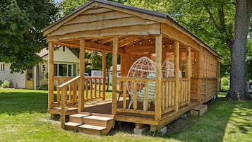A wooden cabin with a porch, steps, and a large woven chair.