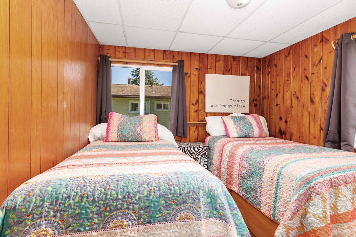 A room with two beds, wooden walls, a window, and a sign that says "This is our happy place."