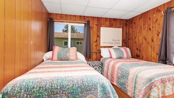 A room with two beds, wooden walls, a window, and a sign that says "This is our happy place."