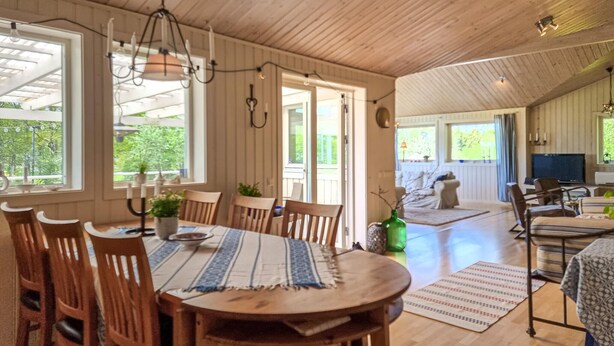 A spacious dining area with wooden tables and chairs, a large window with a view of greenery, and a cozy seating area with a sofa and television. - Beautiful home in Henån with kitchen (Henån)