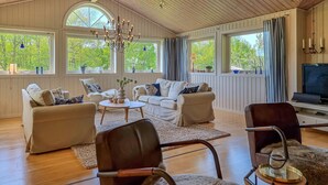 A spacious living room with a large chandelier, multiple seating areas, and large windows offering views of greenery. - Beautiful home in Henån with kitchen (Henån)