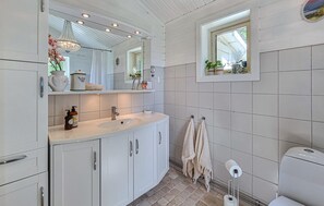 A bathroom with a white sink, mirror, and tiled walls. There is a window with plants, a towel rack, and a toilet. - Beautiful home in Henån with kitchen (Henån)