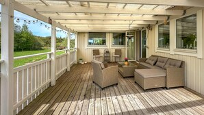 A covered porch with wicker furniture, a glass table, and a view of a green landscape. - Beautiful home in Henån with kitchen (Henån)