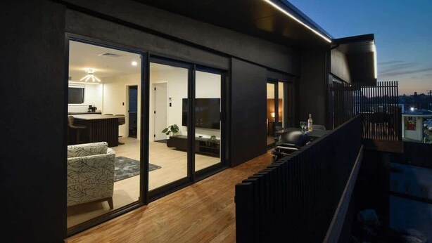 Een modern woongebouw met een balkon en grote schuifdeuren die uitkomen op een woonkamer, met een keuken die door de deuren zichtbaar is.