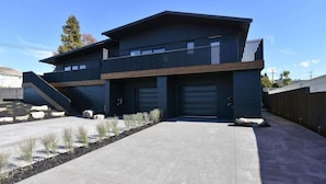 Een modern huis met twee verdiepingen, een plat dak, grote garage deuren en een balkon.