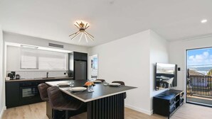 Een moderne keuken met een centraal kookeiland, barstoelen en een eethoek met een televisie.
