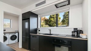 Een moderne keuken met zwarte kastjes, een ingebouwde oven, een vaatwasser en een raam met uitzicht op bomen.