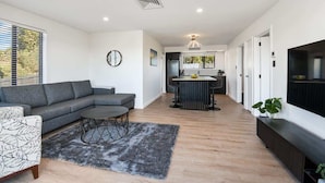 Een moderne woonkamer met een grijze modulaire bank, een ronde salontafel en een televisie op een zwart dressoir.