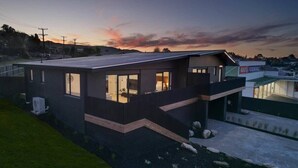 Una casa moderna de dos pisos con grandes ventanales, techo plano y un espacio exterior visible con un camino pavimentado.
