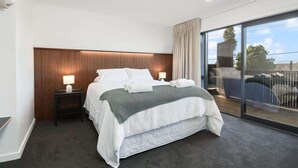 Habitación de hotel moderna con una cama grande, una mesita de noche con lámpara y vistas a través de un amplio ventanal.