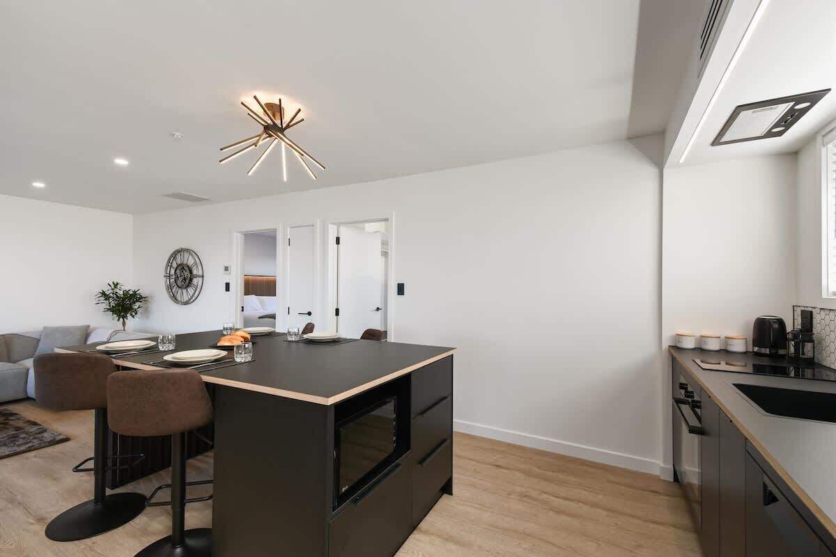 A modern kitchen with a central island, bar stools, a dining area, and a built-in oven.