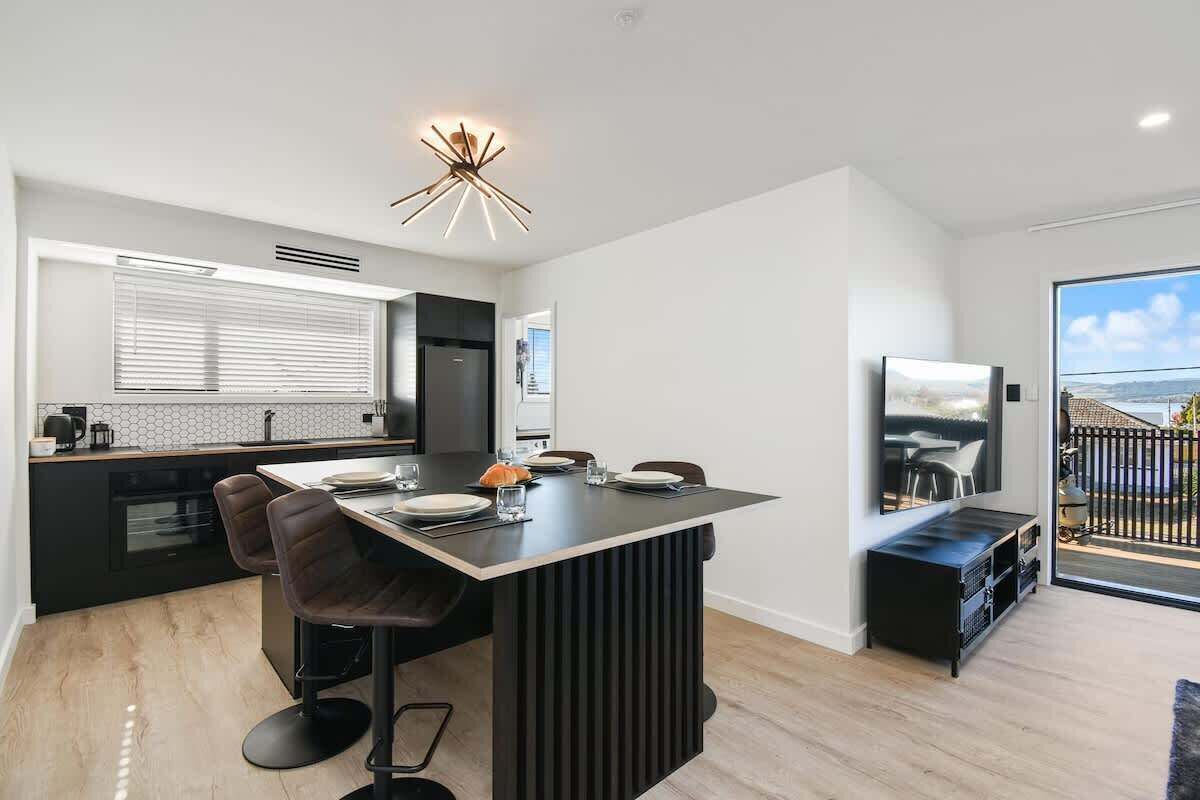 A modern kitchen with a central island, bar stools, and a dining area with a TV.