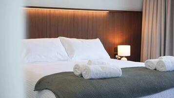 A hotel room with a large bed, a bedside lamp, and rolled towels on the bed.