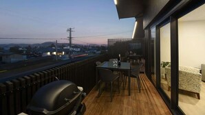 A balcony with a table and chairs, a grill, and a view of the city at dusk. - The Fairlady - Lake Views, Executive, Sleeps 4 (Rotorua)