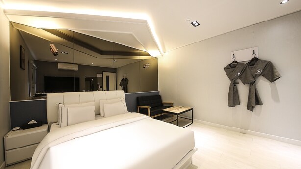 Una habitación de hotel moderna con una cama grande, una zona de estar con sofá y sillones, una mesita y un televisor montado en la pared.