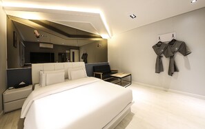 A modern hotel room with a large bed, a seating area with a sofa and armchairs, a small table, and a wall-mounted TV. - Heimishi Hotel Tongyeong (Tongyeong)