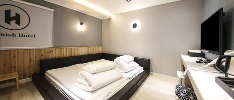 A modern hotel room with a bed, bedside table, and a desk with a chair.