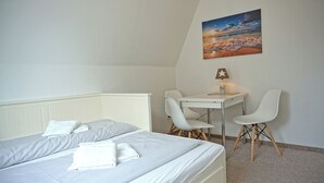Une chambre avec deux lits, un bureau, deux chaises, une lampe et un tableau au mur.