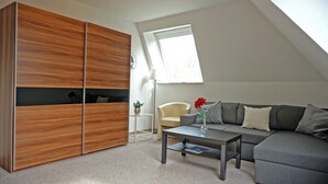 Une chambre de style loft moderne, avec un plafond en pente, une grande armoire, un canapé, une table basse et une petite table d’appoint agrémentée d’une lampe et d’un vase de fleurs.