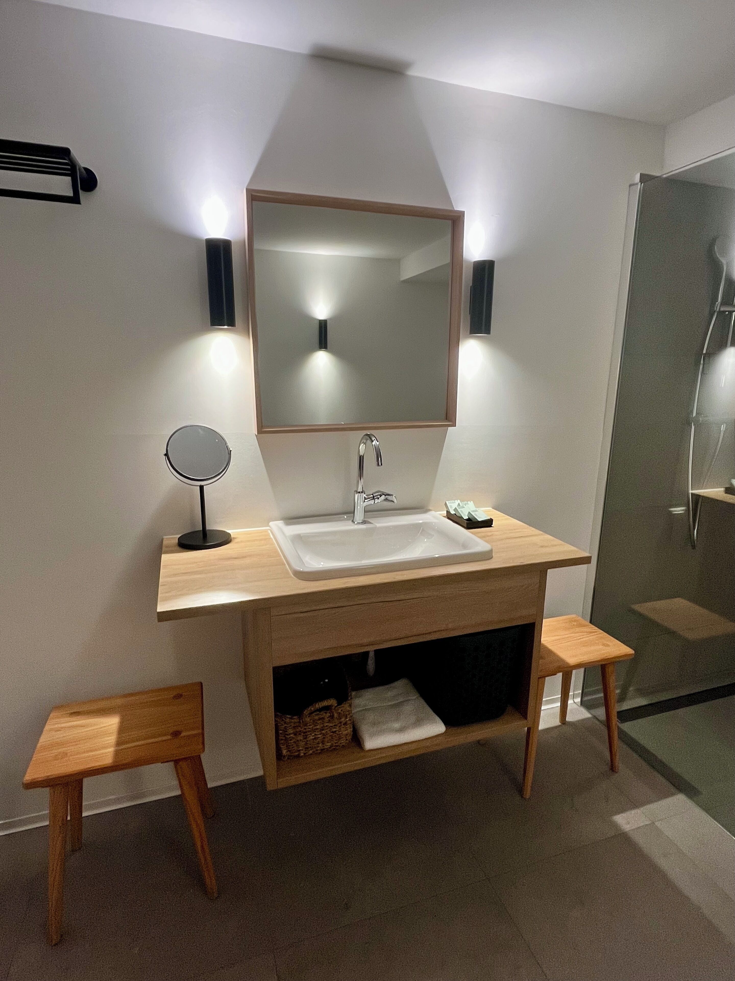 A modern bathroom with a wooden vanity, a large mirror, a sink, and a small stool.