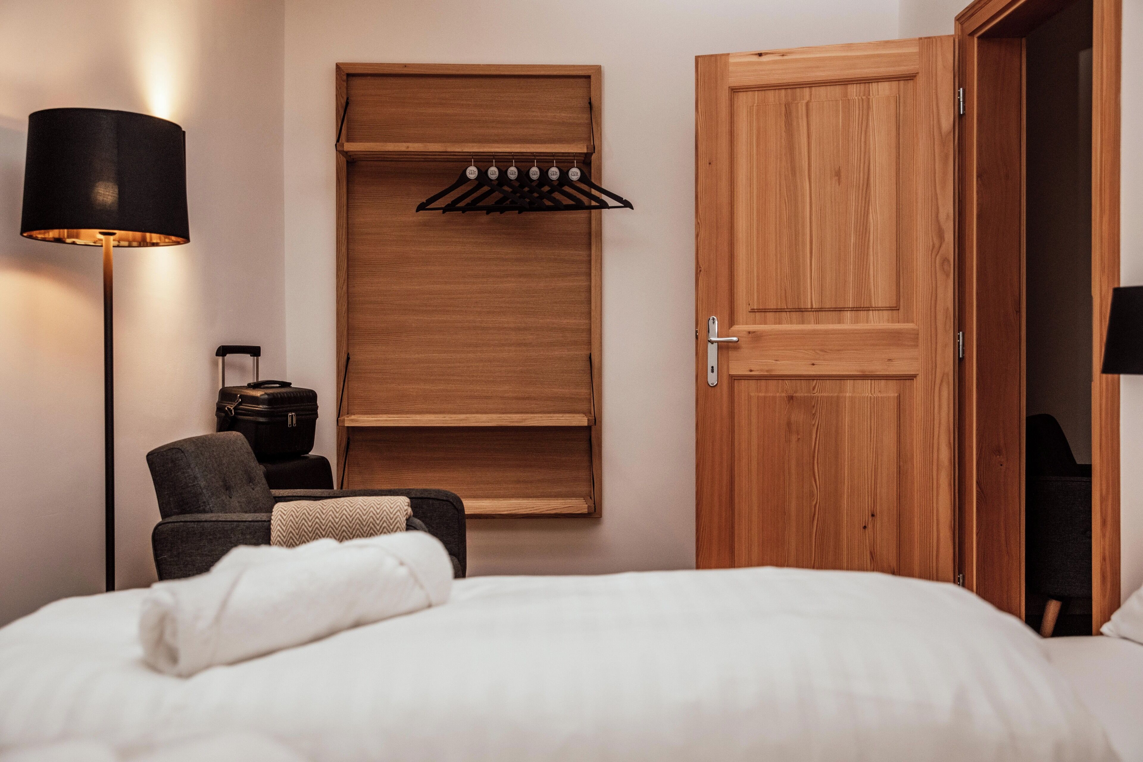 A bedroom with a bed, a chair, a wardrobe, and a hanging coat rack.