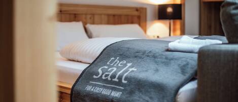 A neatly made bed with a grey blanket and a pillow, a wooden headboard, and a bedside lamp.