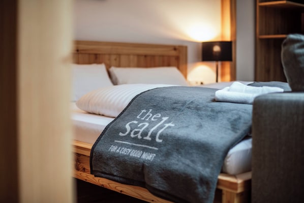 Una cama bien hecha con una manta gris, un cojín y un cabecero de madera, además de una lámpara de noche.
