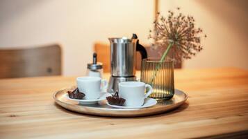 Une table en bois sur laquelle se trouve un plateau avec deux tasses blanches, une cafetière en métal et un vase en verre contenant des fleurs séchées.