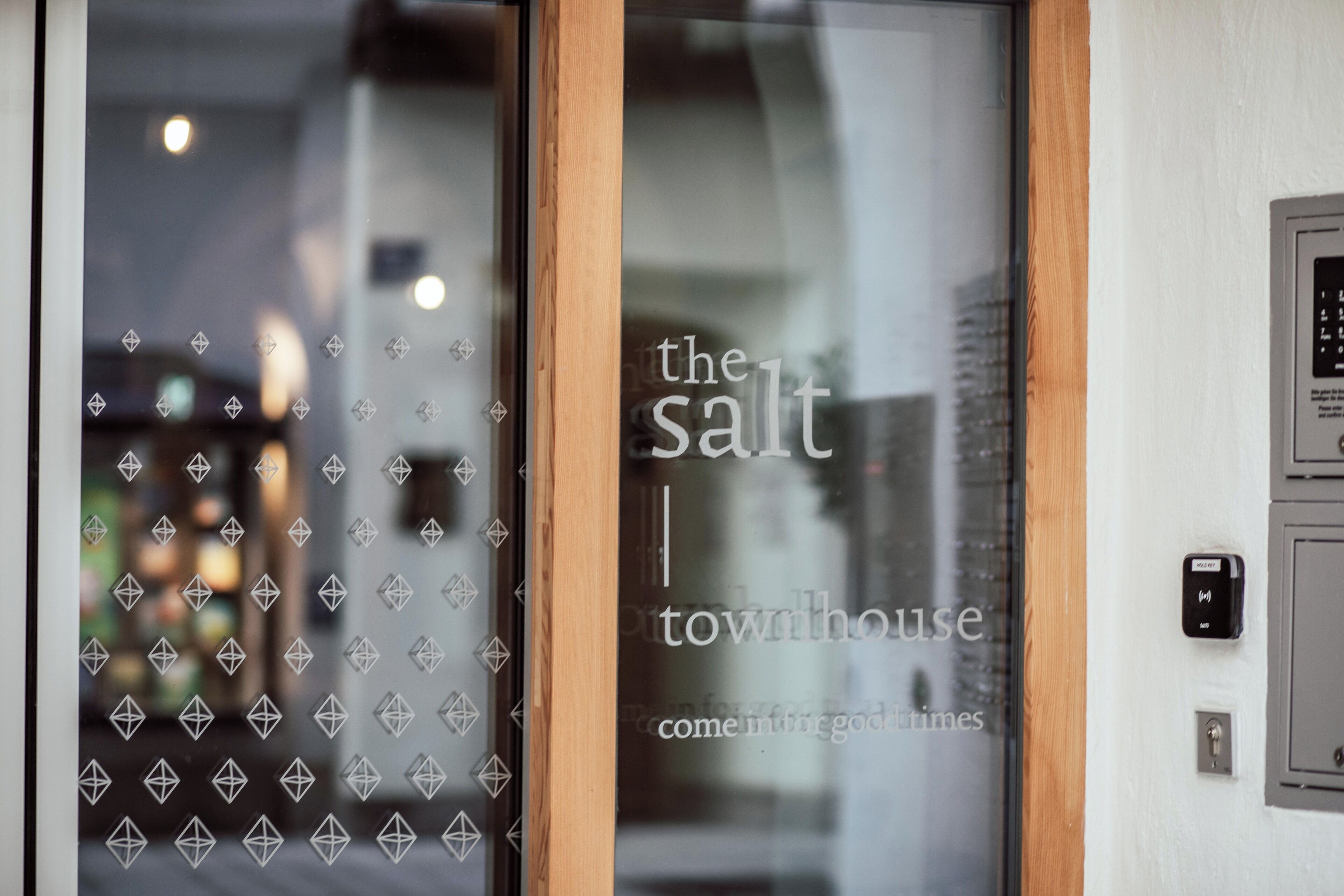 Eine Glastür mit geometrischen Mustern und dem Text "the salt townhouse come in god times".