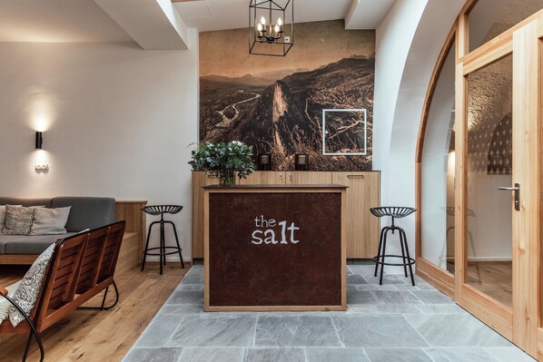 A modern interior with a wooden reception desk labeled "the salt," a gray sofa, and a mural of a mountainous landscape. - the salt townhouse (Hallein)