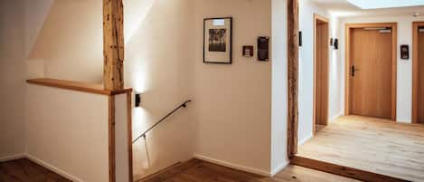 A hallway with wooden flooring, a wooden beam structure, a framed picture, and a door with an emergency exit sign.