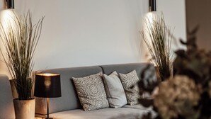 Un salon moderne avec un canapé gris, deux tables d’appoint avec des lampes et des plantes en pot.