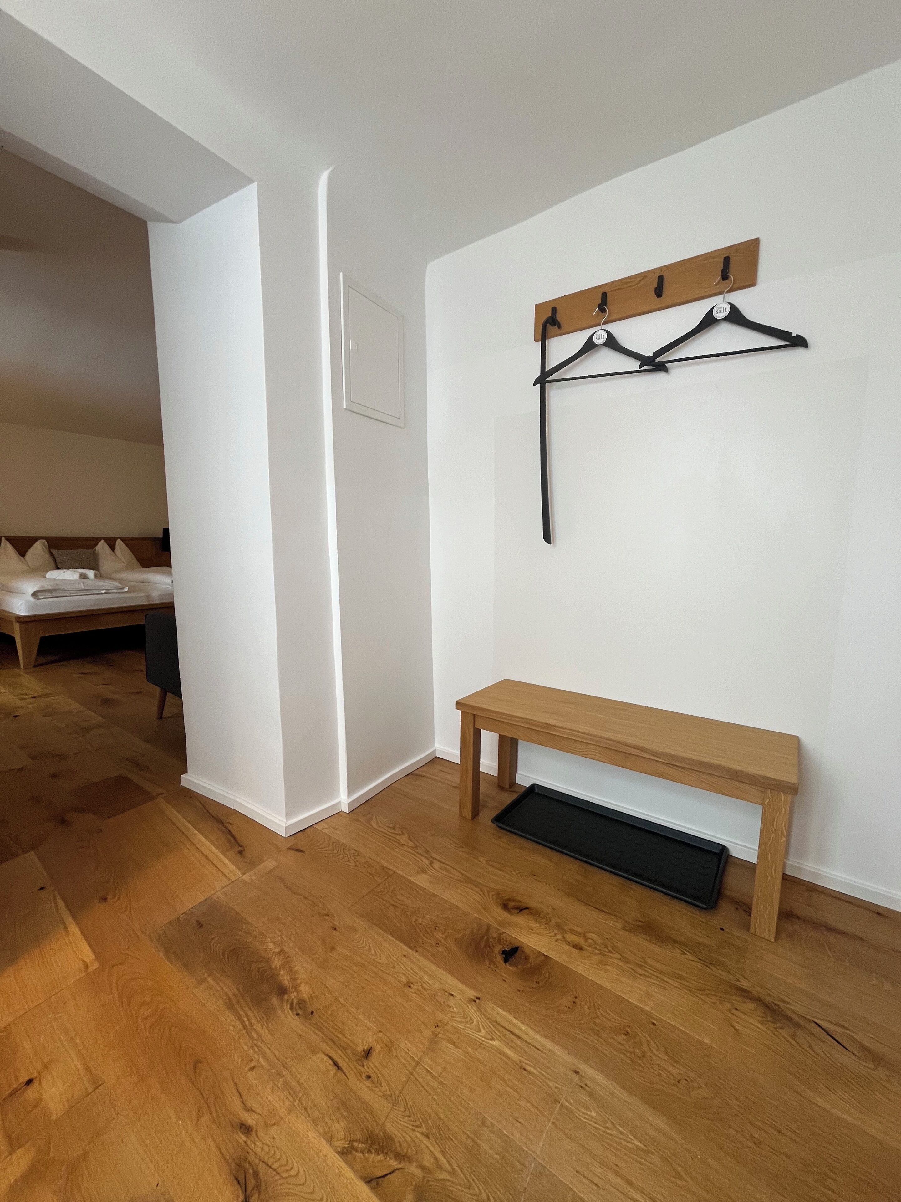 Une chambre d’hôtel avec un banc en bois, un porte-manteau et un lit avec des oreillers.