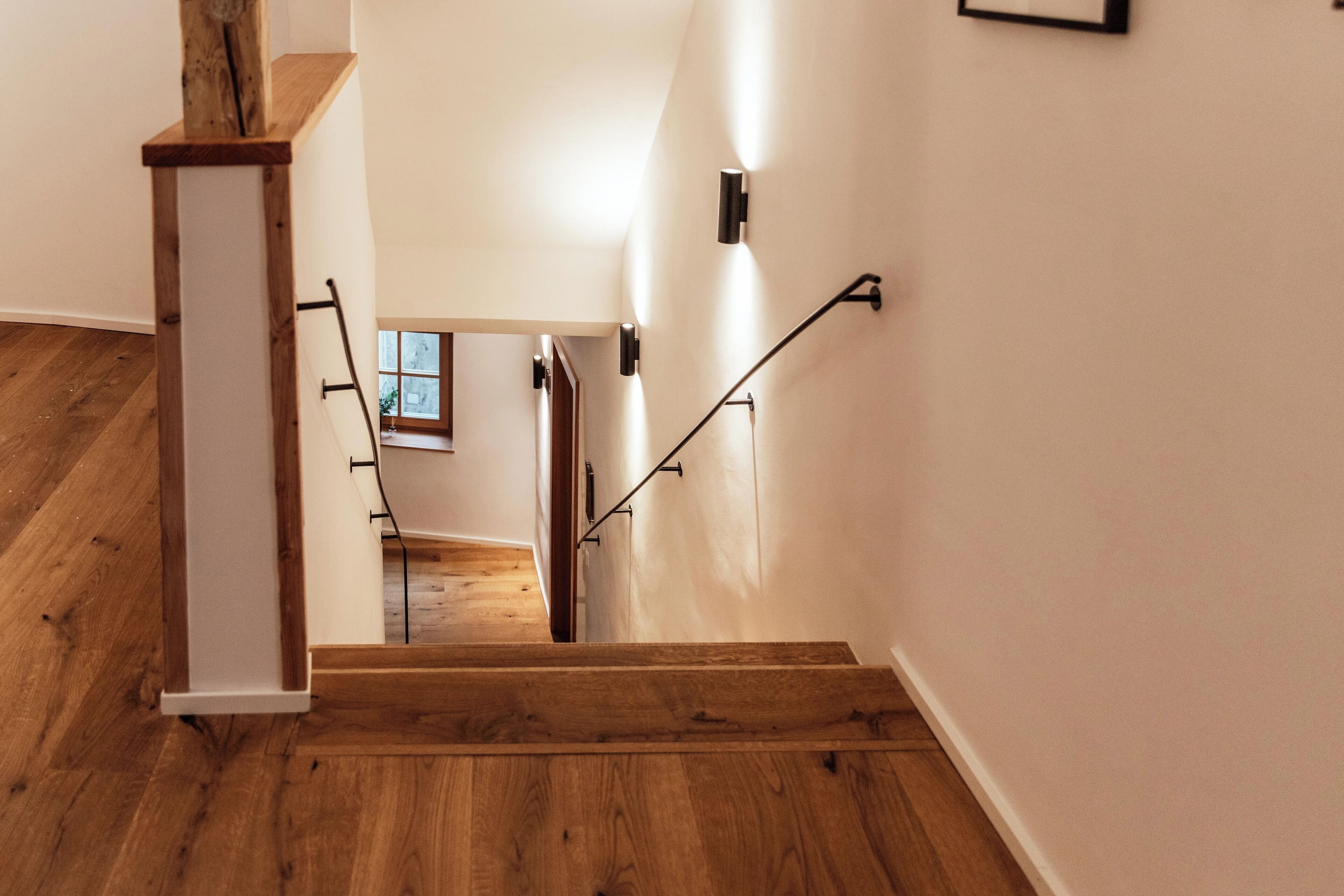 A wooden staircase with a handrail, leading to a room with a window and a door.