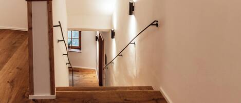 A wooden staircase with a handrail, leading to a room with a window and a door.