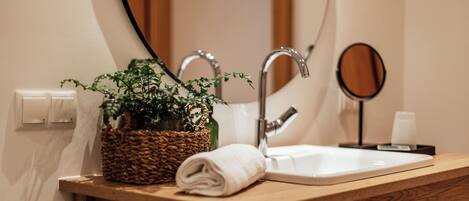 A bathroom with a wooden vanity, a white sink, a mirror, a potted plant, and a towel.