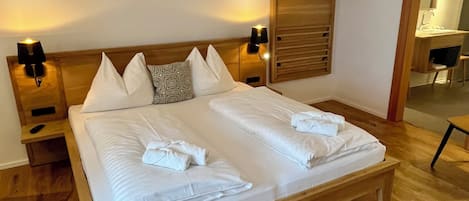 A neatly made bed with white linens and towels, a wooden headboard, two bedside lamps, and a wooden wardrobe with a mirror.