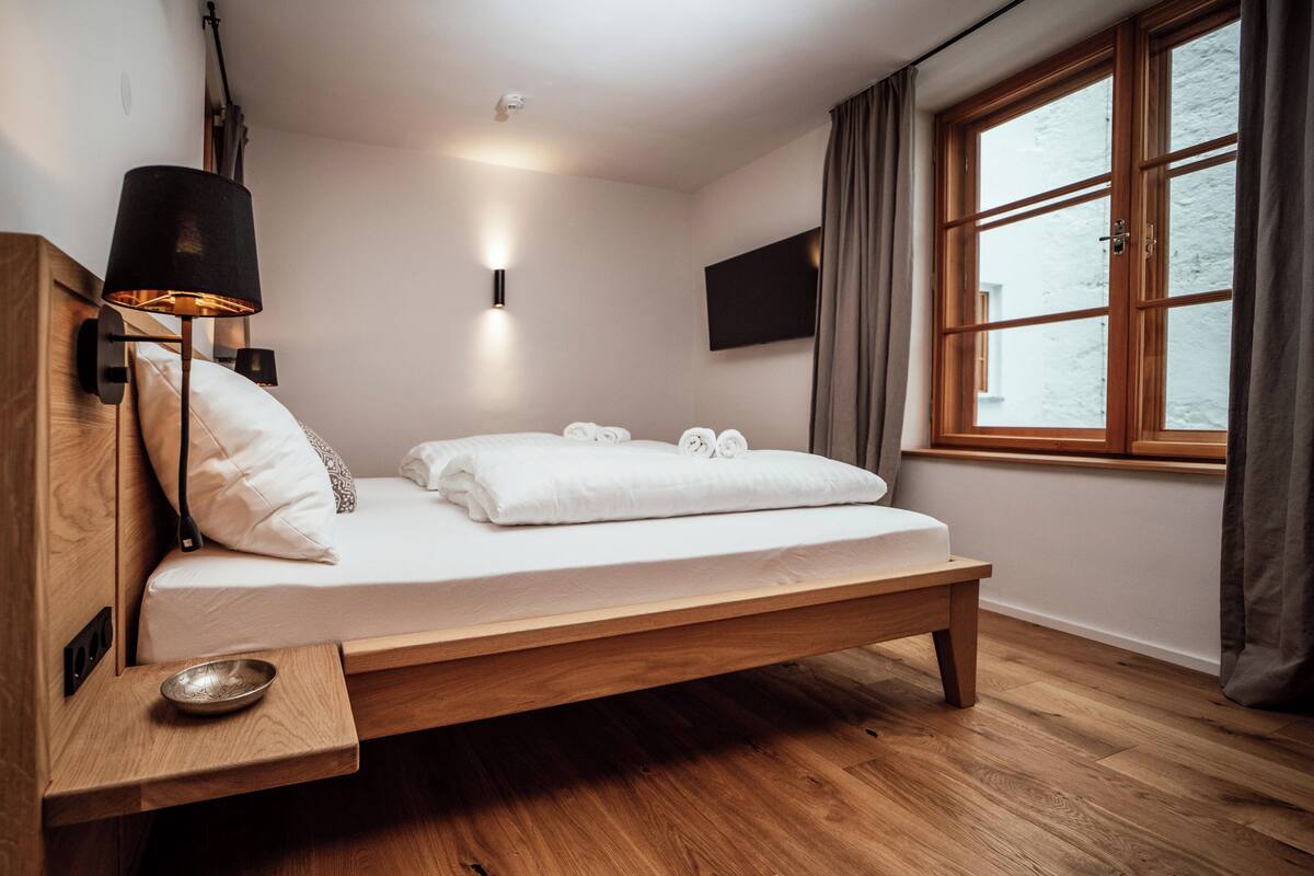 Un dormitorio moderno con cama de madera, lámpara de noche y ventana con cortinas.