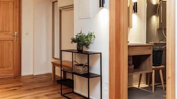 A hallway with wooden flooring, a black metal console table with baskets, a potted plant, and a wooden door.