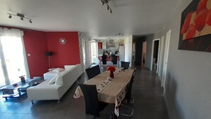 Ampla sala de estar com mesa de jantar, sofá e cozinha ao fundo.