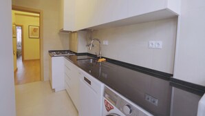 Une cuisine compacte avec des meubles blancs, un plan de travail en acier inoxydable, un lave-vaisselle encastré et un évier avec un robinet.