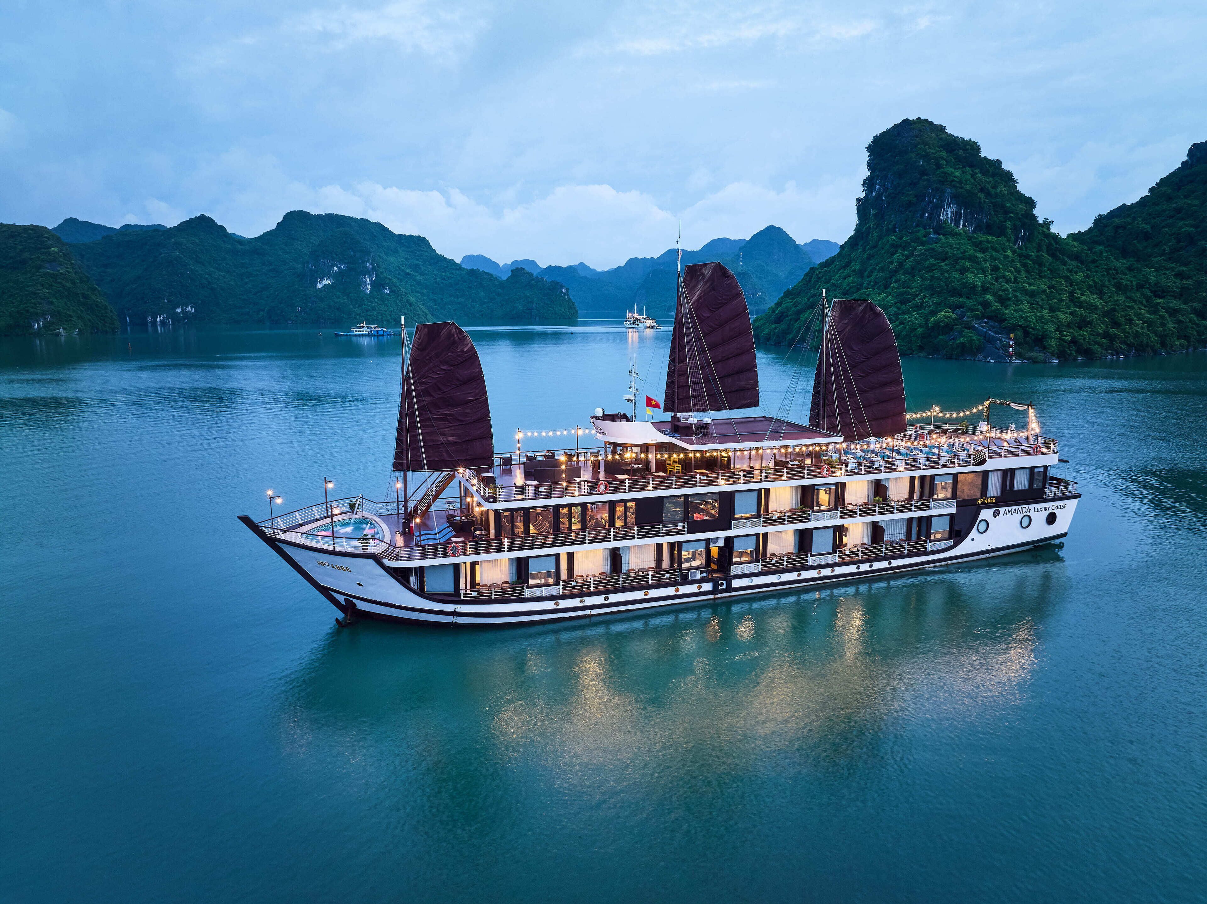 A large, multi-deck boat with a covered dining area and a swimming pool, sailing on a calm lake with mountainous terrain in the background.