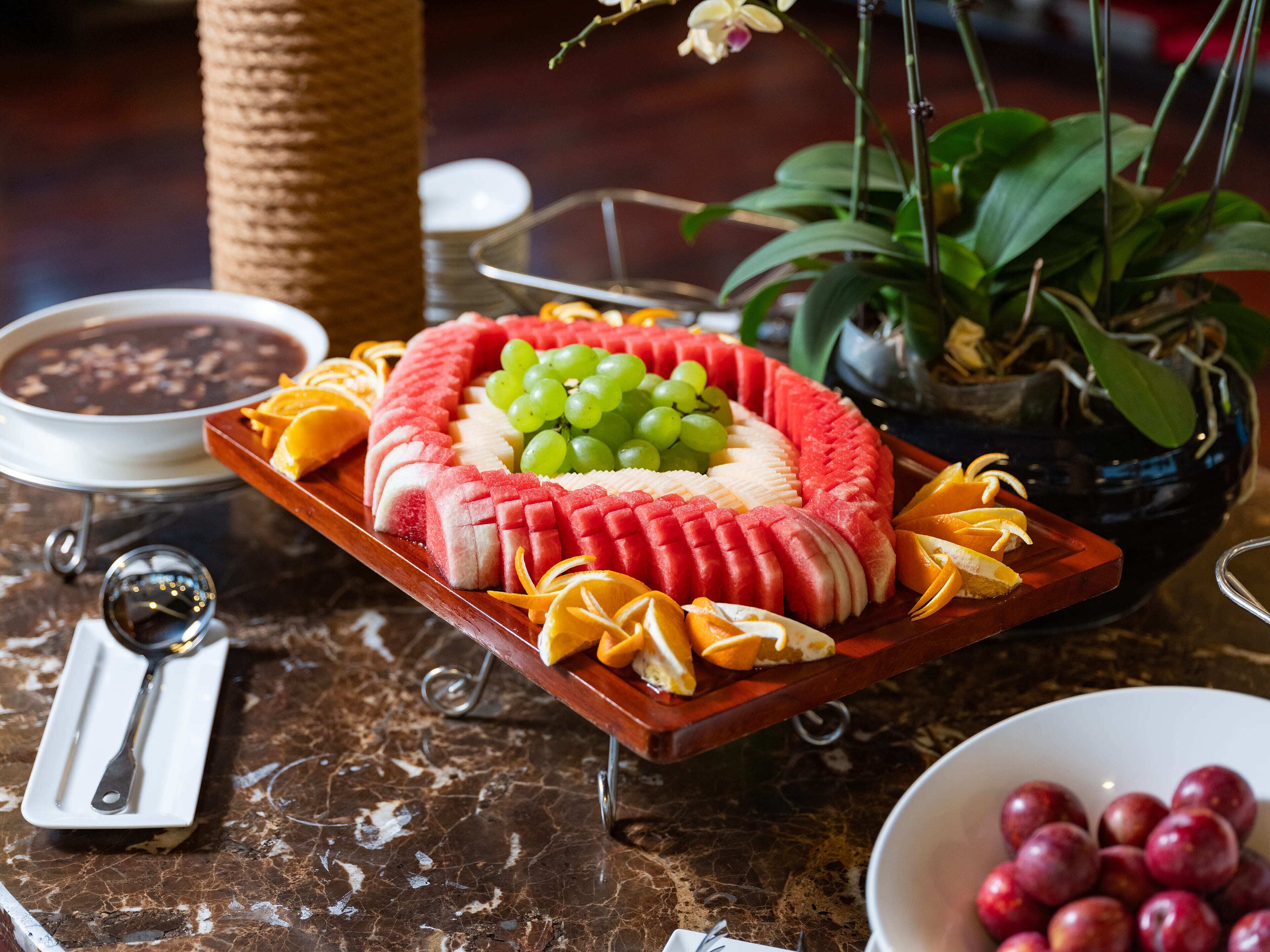 Une assiette de fruits comprenant de la pastèque, des raisins et des oranges, posée sur une table en marbre.