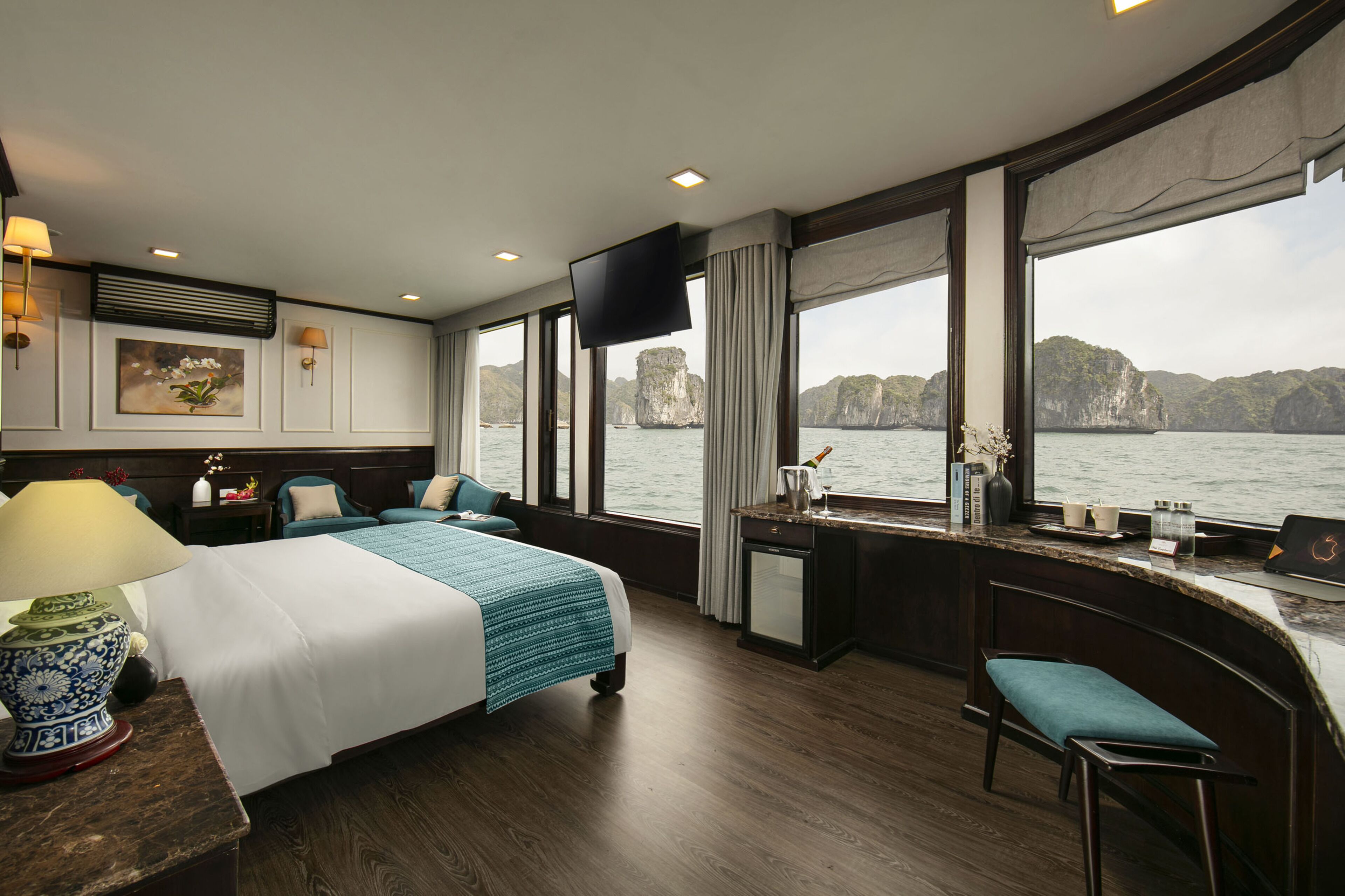 A modern hotel room with a large bed, a desk, and a view of the sea.