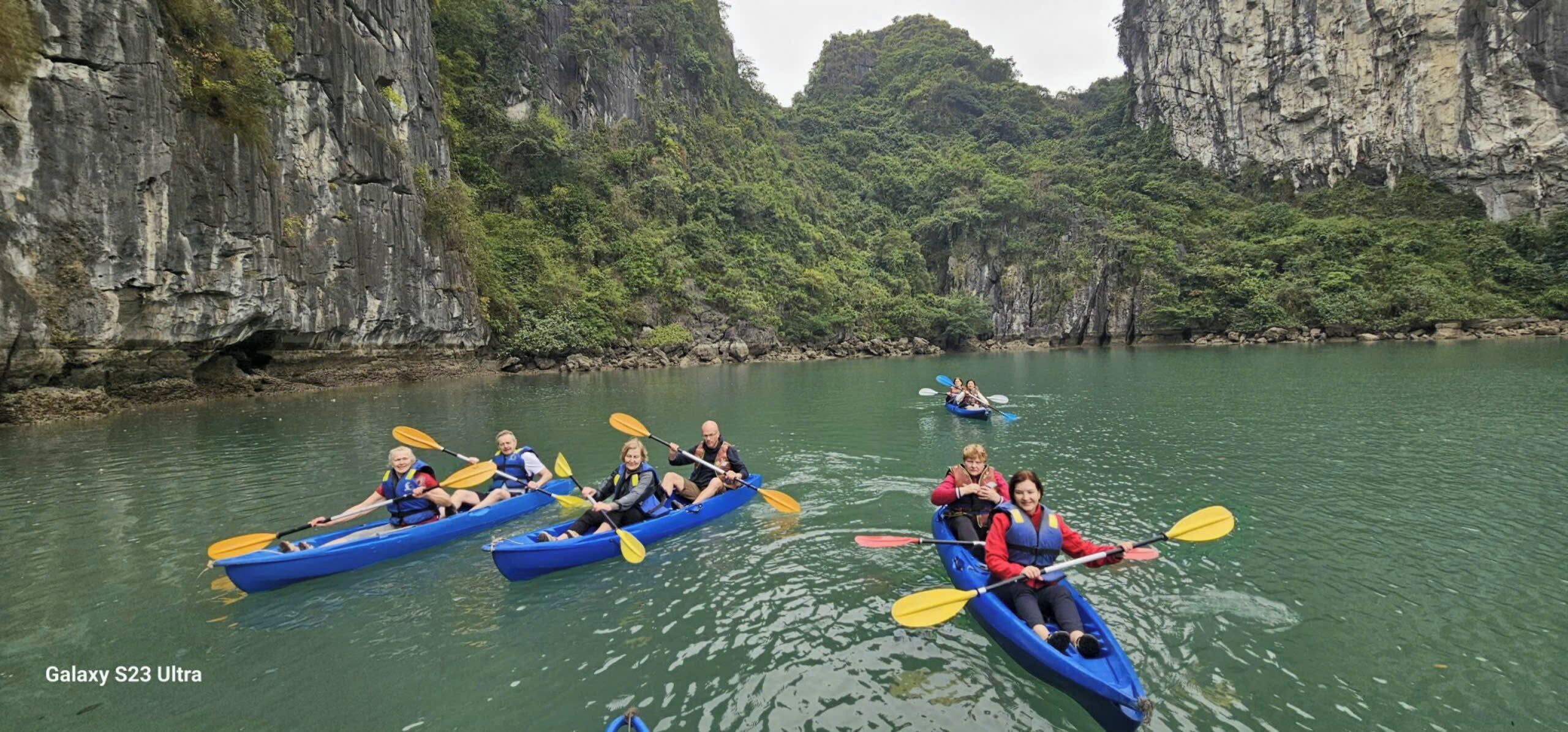 A group of people kayaking on a calm river surrounded by rocky cliffs and lush greenery.